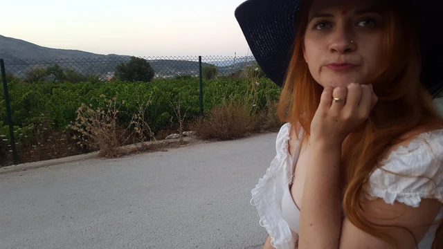 A person in a dark hat resting their chin on a hand beside a country road.