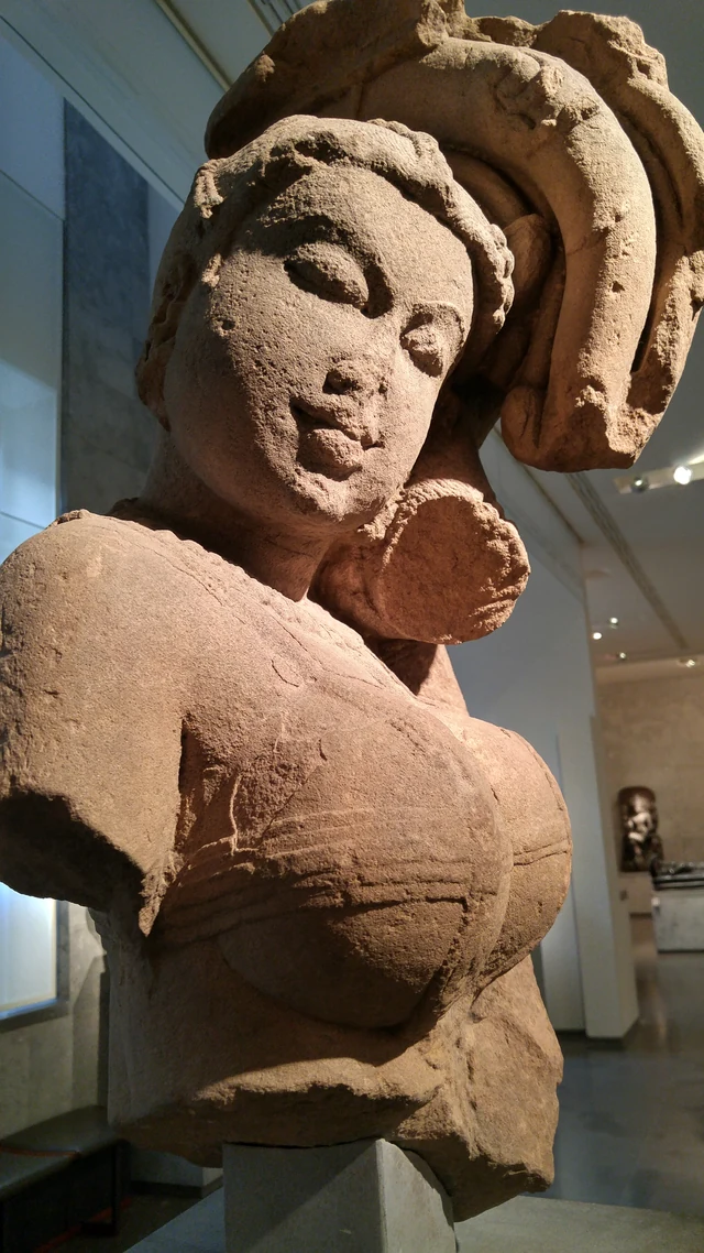 Close view of a stone figure with an ornate headdress, lit from the side.