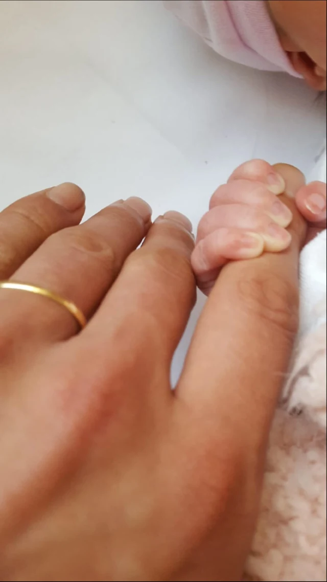 A small hand holding an adult finger above pale fabric.