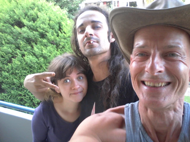 Three people posing together outdoors in front of green foliage.