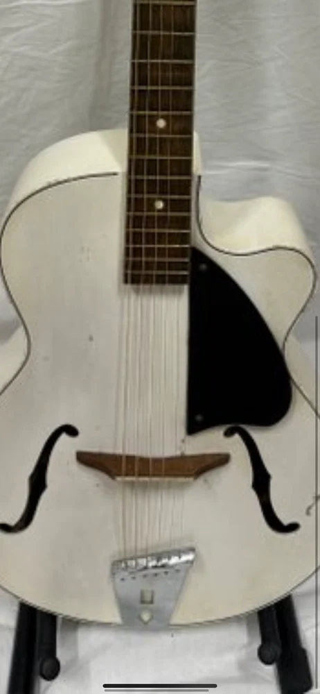 Close view of a white archtop guitar body, strings, bridge and black pickguard.